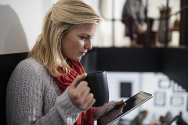 Junge Frau liest auf einem digitalen Tablet und hält eine Tasse Kaffee - ZEF10372