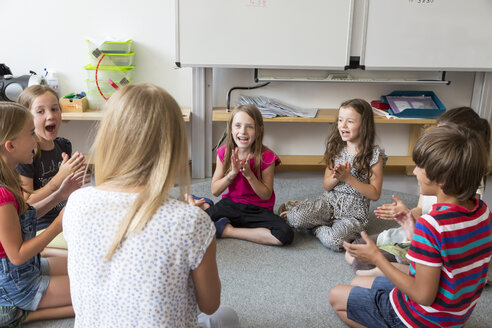 Lehrer und Schüler sitzen auf dem Boden ihres Klassenzimmers und singen und klatschen in die Hände - SARF02894