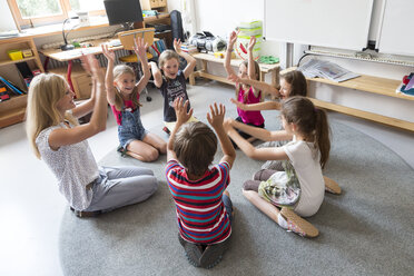 Lehrer und Schüler sitzen im Kreis auf dem Boden ihres Klassenzimmers und heben die Hände - SARF02895