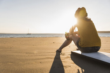 Teenager-Mädchen sitzt auf einem Surfbrett und hört Musik am Strand - UUF08529