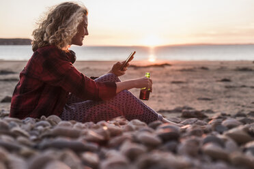 Teenager-Mädchen entspannt sich am Strand und benutzt ein Smartphone - UUF08556