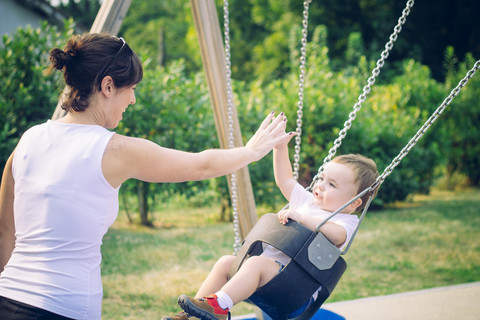 Baby boy sitting on a swing watching his mother stock photo