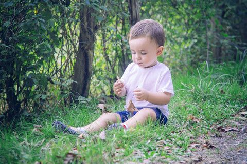 Baby boy sitting on the grass playing with leaves stock photo