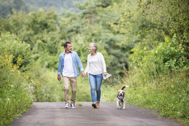 Glückliches Seniorenpaar beim Spaziergang mit Hund in der Natur - HAPF00877