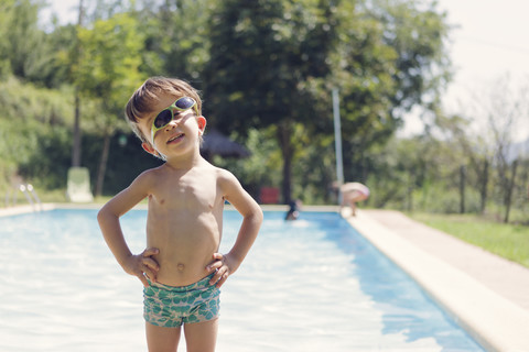 Porträt eines kleinen Jungen mit Sonnenbrille, der vor einem Schwimmbad steht, lizenzfreies Stockfoto