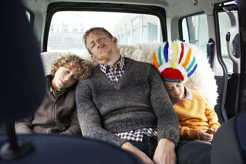 Sleeping father sitting in car on back seat with his sons stock photo