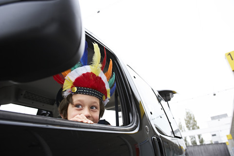 Junge mit Federkopfschmuck schaut aus dem Autofenster, lizenzfreies Stockfoto