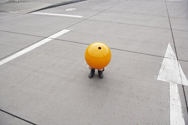 Little girl crouching in street, hiding under orange sphere - FSF00488