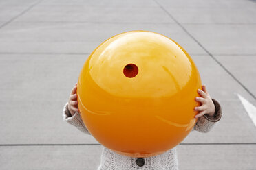 Kleines Mädchen steht auf der Straße und versteckt sich unter einer orangefarbenen Kugel - FSF00490