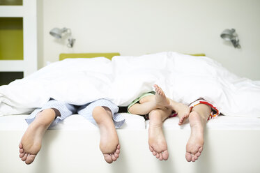 Family lying in bed of hotel room showing their foot soles - FSF00494