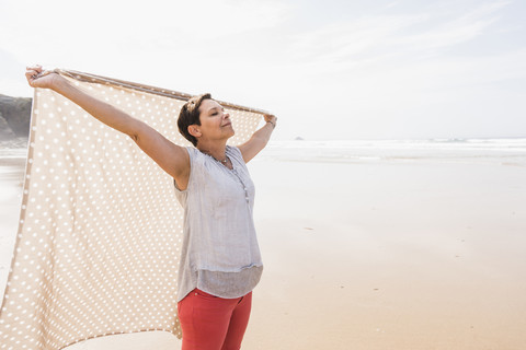 Ältere Frau am Strand hebt eine Decke, lizenzfreies Stockfoto