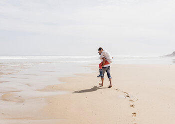 Mature man carrying wife piggyback on the beach - UUF08576