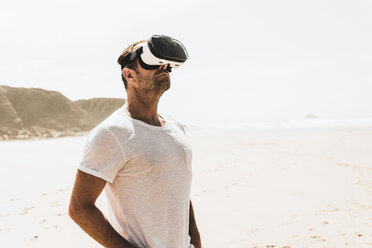 Mature man standing on the beach wearing VR glasses - UUF08597
