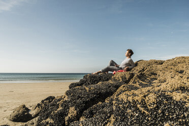 Mature woman relaxing on rock at the beach - UUF08601