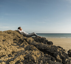 Mature woman relaxing on rock at the beach - UUF08602