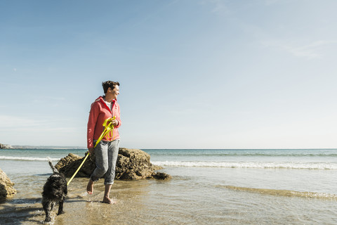 Ältere Frau geht mit Hund am Meer spazieren, lizenzfreies Stockfoto