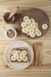 Toast mit Dulce de Leche, Bananenscheiben und Sesamsamen auf Holzteller und Tisch - RTBF00376