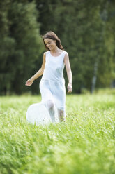 Happy woman wearing white summer dress walking on a meadow - MAEF12019