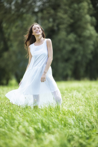 Glückliche Frau im weißen Sommerkleid auf einer Wiese stehend, lizenzfreies Stockfoto