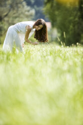 Glückliche Frau im weißen Sommerkleid pflückt Blumen auf einer Wiese - MAEF12023