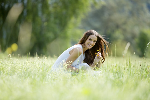 Glückliche Frau, die auf einer Wiese hockt und Blumen pflückt, lizenzfreies Stockfoto