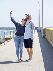 Frankreich, Bretagne, Finistere, glückliches junges Paar macht Selfie mit Smartphone am Hafen - LAF01732