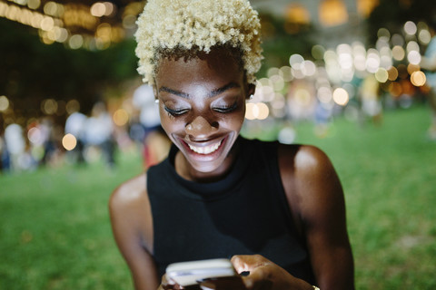 Young woman sitting in a park at night looking at cell phone stock photo