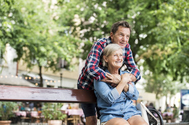 Älterer Mann, der seine Frau umarmt, die auf einer Bank sitzt - HAPF00901