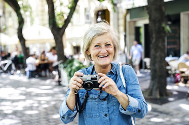 Porträt einer lächelnden älteren Frau mit Kamera - HAPF00940