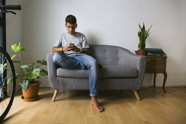 Jugendlicher sitzt zu Hause auf der Couch und schaut auf sein Handy - EBSF01763