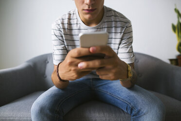 Teenage boy sitting on couch at home using cell phone - EBSF01764