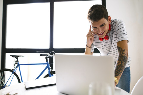 Lächelnder Teenager am Telefon mit Blick auf den Laptop, lizenzfreies Stockfoto