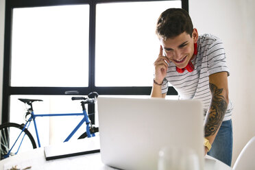 Smiling teenage boy on the phone looking at laptop - EBSF01781