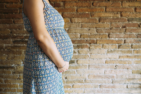Schwangere Frau, die an einer Mauer steht, lizenzfreies Stockfoto