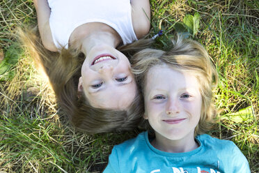 Portrait of brother and little sister lying on a meadow looking up to camera - SARF02903