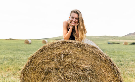 Porträt eines lächelnden blonden Teenagers auf einem Strohballen liegend - MGOF02436
