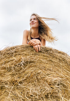 Porträt eines lächelnden blonden Teenagers auf einem Strohballen liegend - MGOF02439