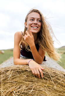Porträt eines lächelnden blonden Teenagers auf einem Strohballen liegend - MGOF02440