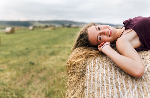 Porträt eines lächelnden blonden Teenagers auf einem Strohballen liegend - MGOF02441