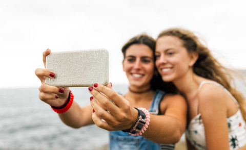 Zwei beste Freunde machen ein Selfie mit Smartphone an der Küste, Nahaufnahme, lizenzfreies Stockfoto