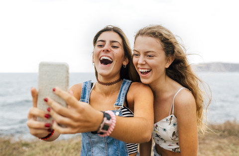 Zwei beste Freunde machen ein Selfie mit Smartphone an der Küste, lizenzfreies Stockfoto
