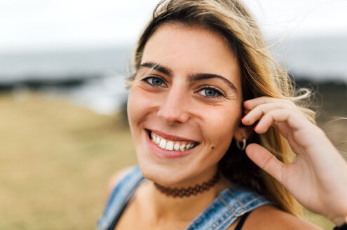 Porträt eines lächelnden Teenagers an der Küste sitzend - MGOF02451