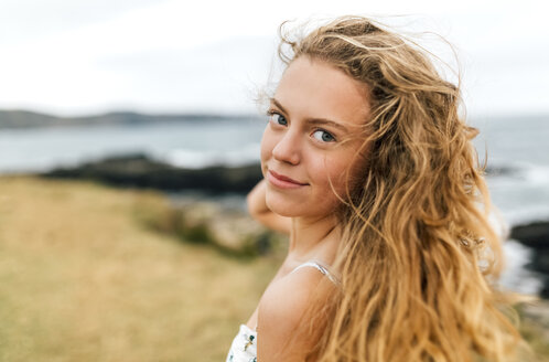 Porträt eines lächelnden blonden Teenagers mit wehendem Haar an der Küste - MGOF02453