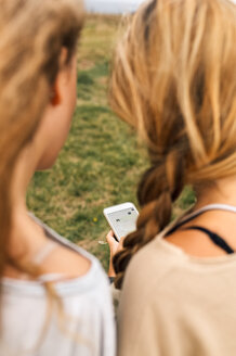 Rückenansicht von zwei Teenager-Mädchen, die auf ihr Smartphone schauen - MGOF02454