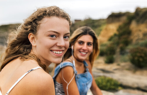 Lächelndes blondes Teenager-Mädchen hört mit ihrer besten Freundin Musik - MGOF02456