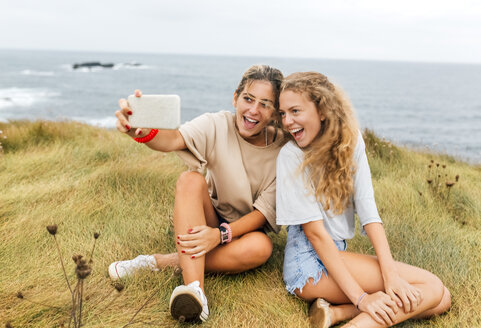 Zwei schreiende Teenager-Mädchen machen ein Selfie an der Küste - MGOF02464