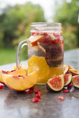 Ein Glas Wasser mit Orangenscheiben, Feigen, Granatapfelkernen, Nektarinen und Pflaumen, lizenzfreies Stockfoto