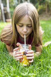Mädchen liegt auf einer Wiese und trinkt Wasser mit verschiedenen Früchten - SARF02911