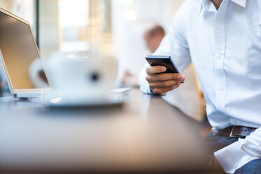 Nahaufnahme eines Geschäftsmannes mit Mobiltelefon und Laptop in einem Cafe - DIGF01230