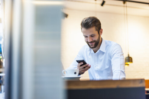 Lächelnder Geschäftsmann mit Blick auf sein Handy in einem Café - DIGF01231
